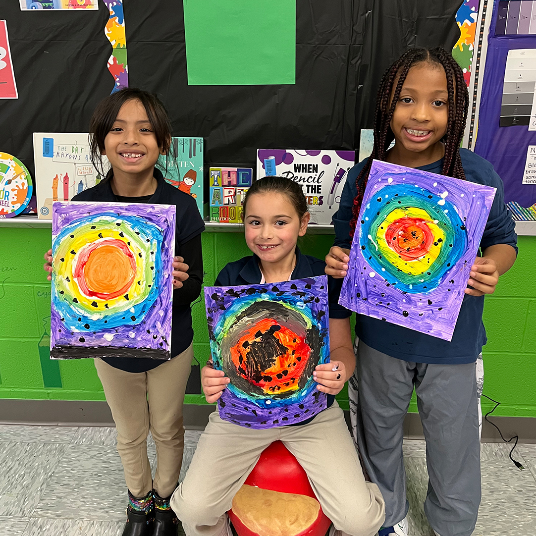 Three children showcasing their artwork.