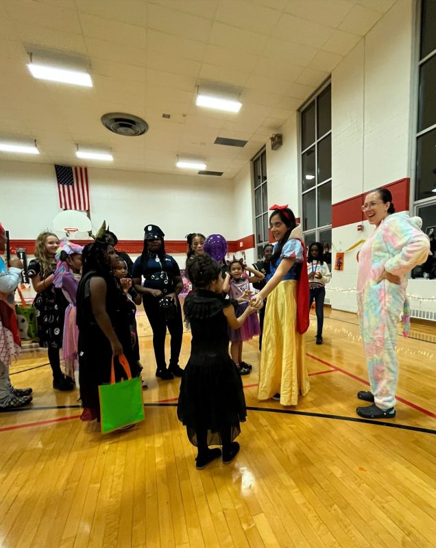 A group of children and two adults in a gymnasium wearing Halloween costumes.