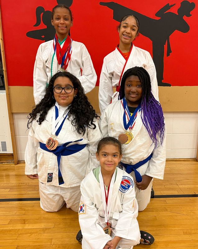 Five girls wearing karate attire posing with their metals.